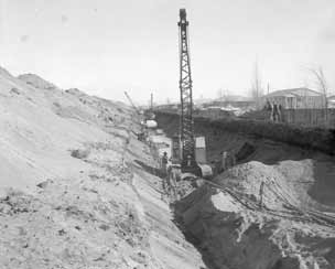 Large crane and men digging and laying sewer mains.